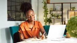 Business woman at desk, writing on a piece of paper in front of her computer.